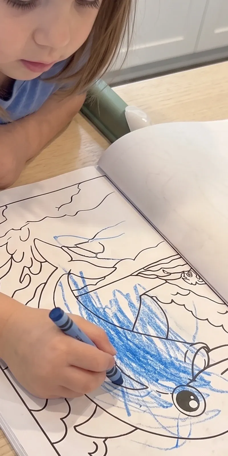 A girl coloring a dolphin page with a blue crayon